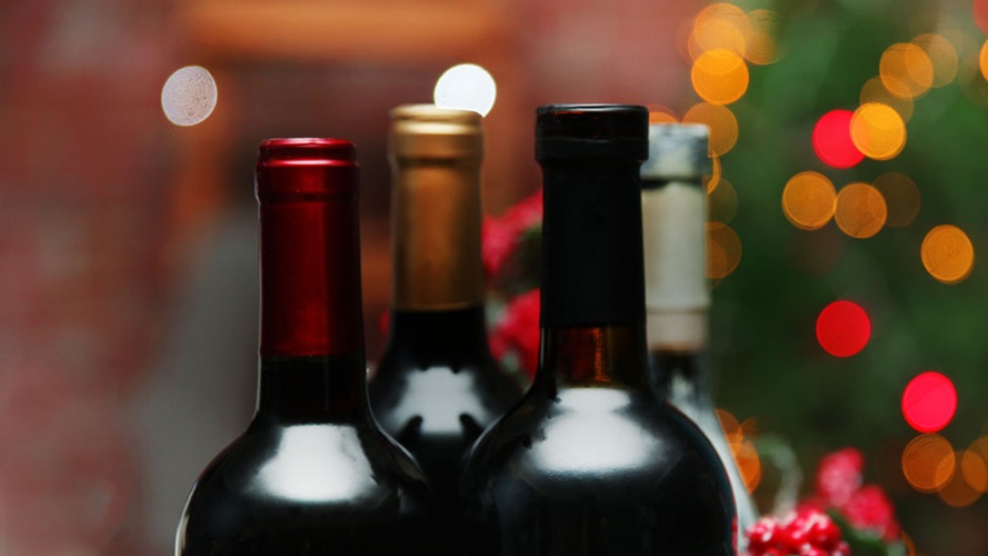The necks and tops of three bottles of wine in front of a Christmas tree.