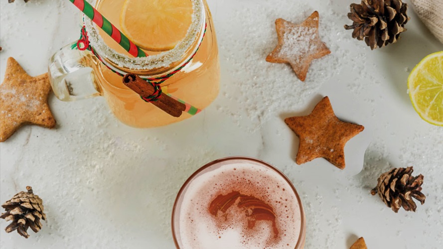 A top view of mixed holiday drink in a mason jar on a table that is decorated with star-shaped cookies, pinecones and fake snow. 