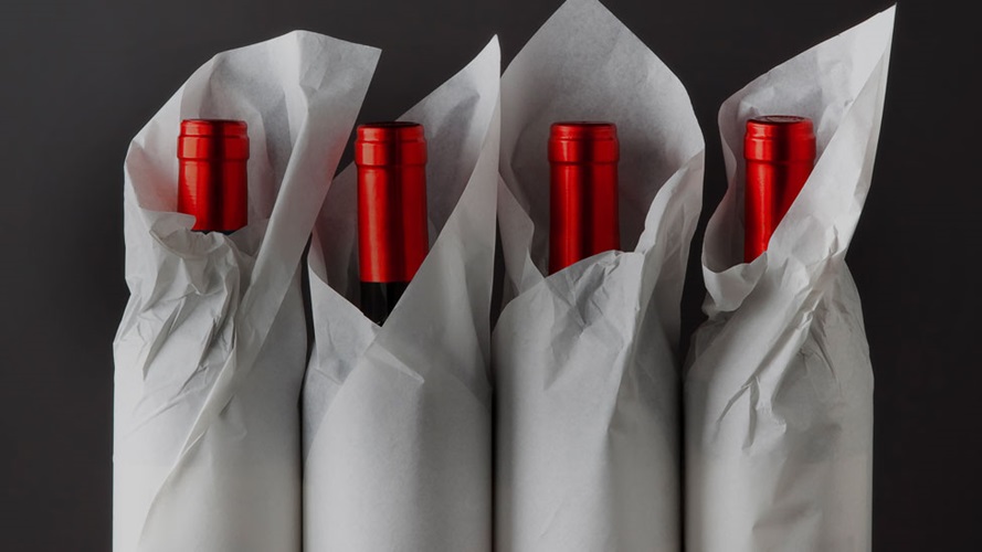 Four bottles of wine loosely wrapped with paper.