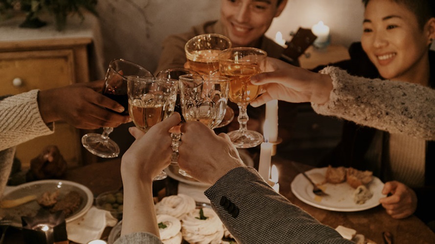 Five people toasting goblet glasses over a table with mostly empty plates. 