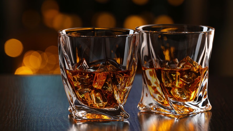 Two glasses of whisky on the rocks sitting on a table. 