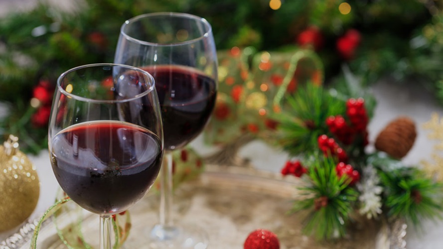 Two glasses of red wine on a gold platter on a table with Christmas decorations. 