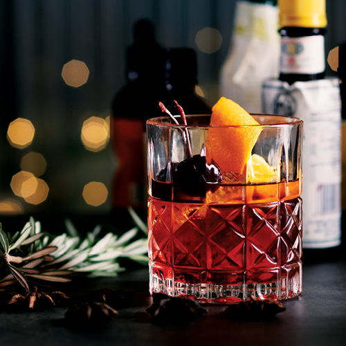 A glass filled with red translucent liquid, black cherries, and peach slices. 