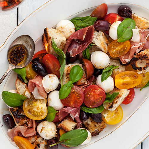 A large serving dish of tomatoes, basil, prosciutto and mozzarella balls