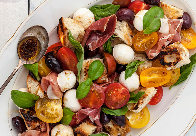 A large serving dish of tomatoes, basil, prosciutto and mozzarella balls