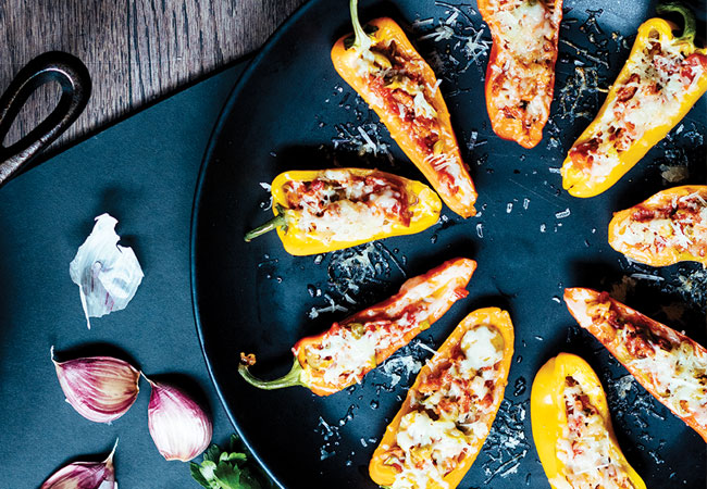 Yellow peppers halved and stuffed, topped with melted cheese on a black plate