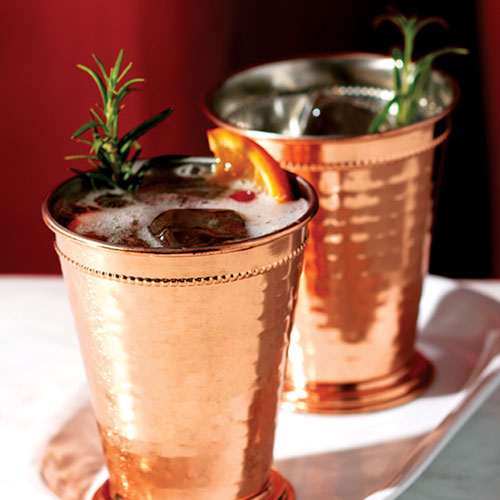 Cranberry mocktail in a copper tin cup with rosemary and orange slice garnish. 