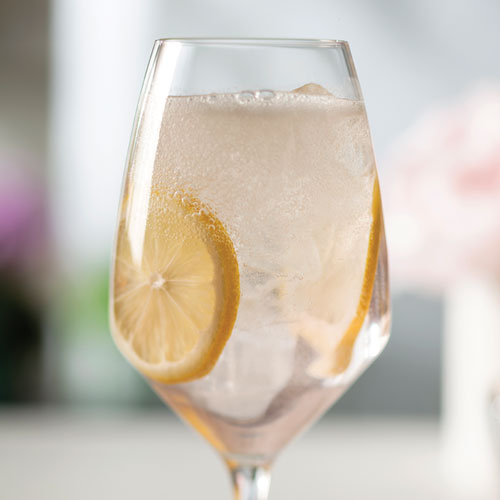 Fizzing, light pink cocktail in a wine glass with ice cubes and lemon slices. 