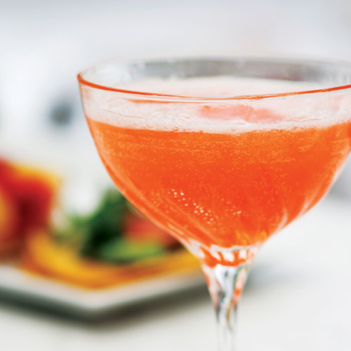 Sparkling, orange cocktail with blurred food in the background. 