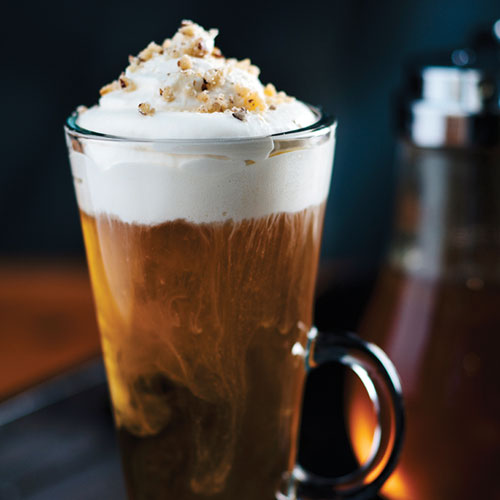 Glass mug with whip cream melting into the cocktail, topped with crushed macadamia nuts. 
