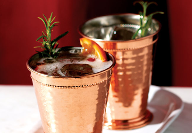 Cranberry mocktail in a copper tin cup with rosemary and orange slice garnish. 