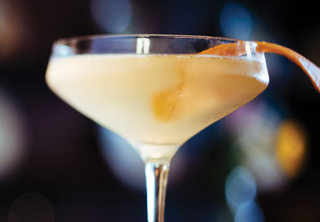 A light lemon colour, sparkling cocktail with an orange grind for garnish. 