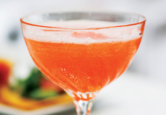 Sparkling, orange cocktail with blurred food in the background. 