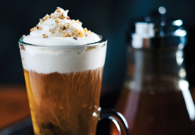 Glass mug with whip cream melting into the cocktail, topped with crushed macadamia nuts. 