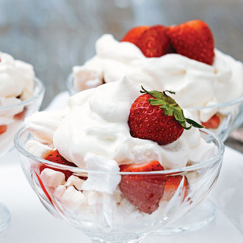 A bowl of strawberries topped with meringue and whipping cream