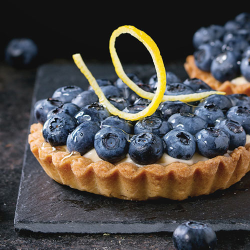 A tart shell topped with fresh blueberries and a lemon twist