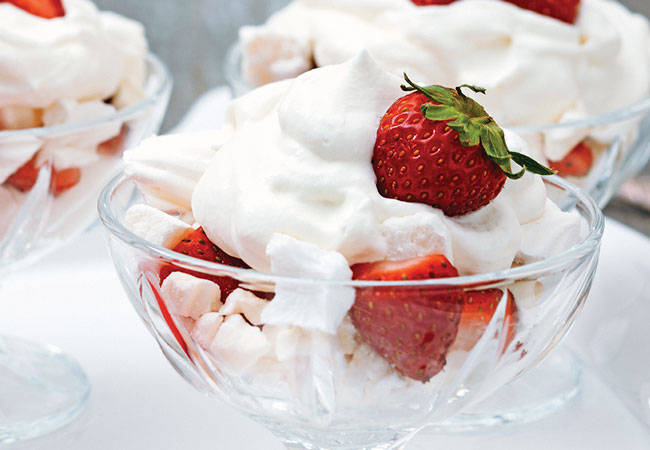 A bowl of strawberries topped with meringue and whipping cream
