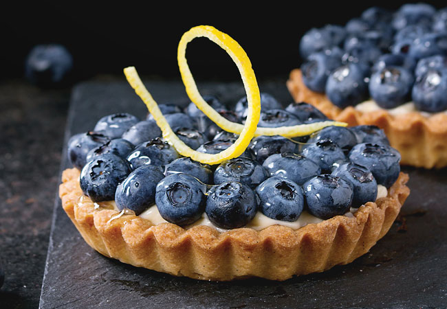 A tart shell topped with fresh blueberries and a lemon twist
