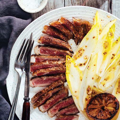 Sliced charred steak with a side of endive salad