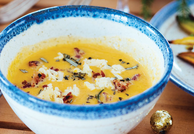 A bowl of squash soup topped with bacon and rosemary