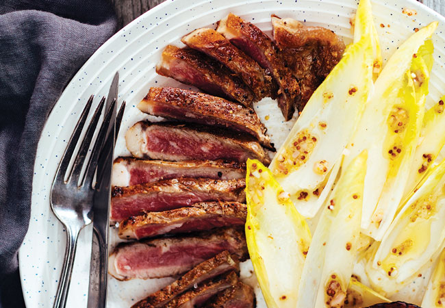 Sliced charred steak with a side of endive salad