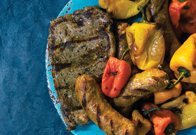 A grilled steak with chorizo and red and yellow peppers