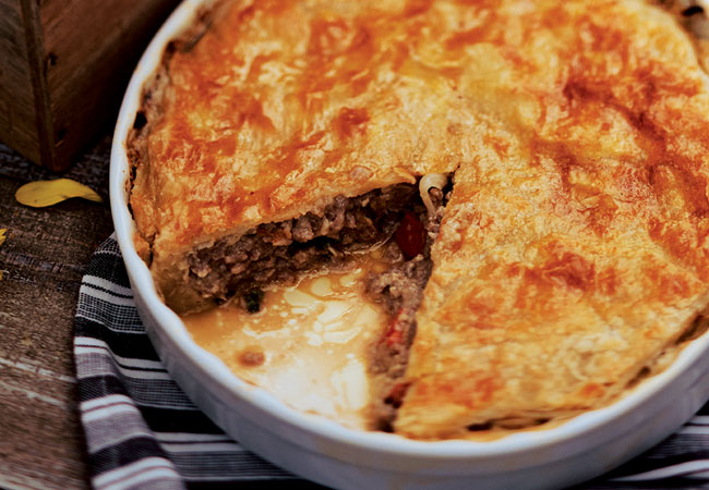 A golden pie with meat and vegetable filling with 1 slice out