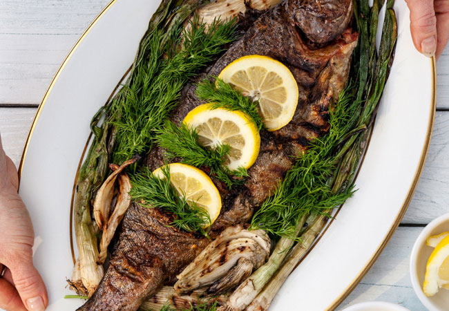 A whole trout on a platter topped with lemon wheels and fresh herbs