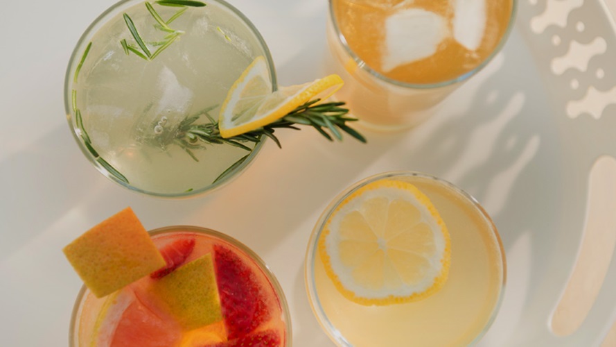 Four different summer citrus drinks in different shades of green and orange.