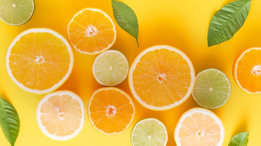Multiple orange and lime slices scattered and intermixes with green citrus leaves.