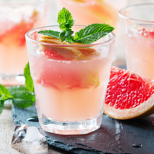 A cocktail glass with grapefruit slices and mint springs.