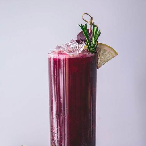 Cocktail glass with a beet red cocktail, garnished with a lemon and rosemary.