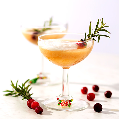 A stemmed cocktail glass filled with a caramel coloured liquid and garnished with a cranberry and sprig of rosemary. 