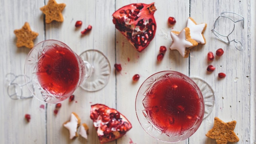 2 red cocktails on a wooden table with star shaped cookies and pomegranate seeds.