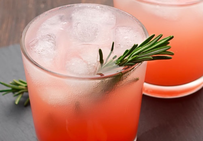 A cocktail with a red liquid garnished with a sprig of rosemary.