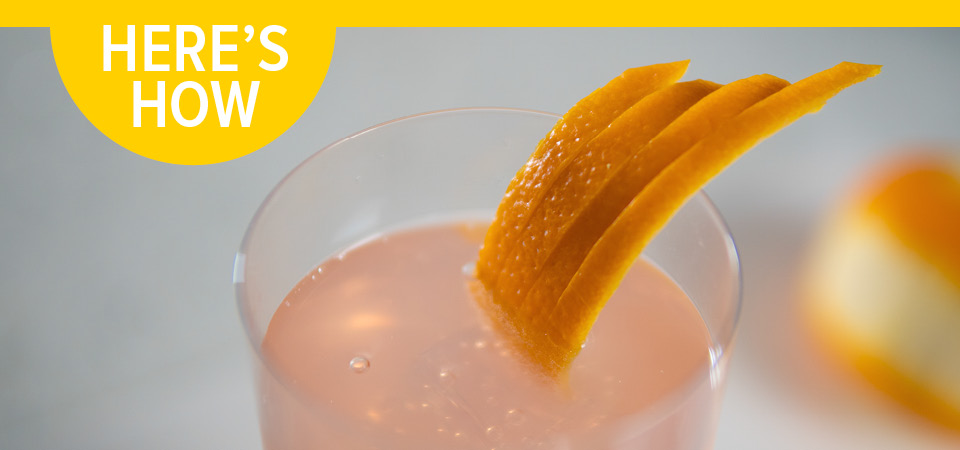 A glass filled with a pink liquid garnished with an orange fan and the headline "Here's How".