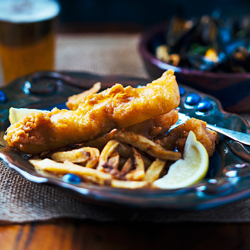 A piece of Wheat Beer Battered Fish on a plate with fries