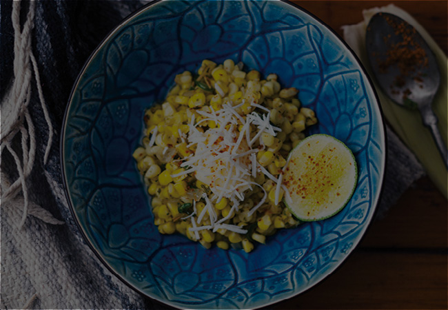 Blue bowl of corn with cheese in top and lime wedge. 