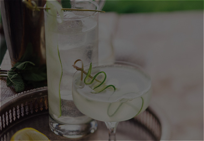 A highball glass and coupe glass on a tray with the cucumber fizz mocktail and a cucumber ribbon garnish