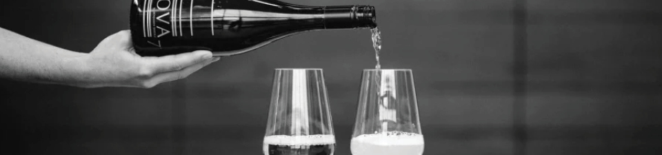 Black and white photo of a person pouring Nova 7 from a bottle into wine glasses.