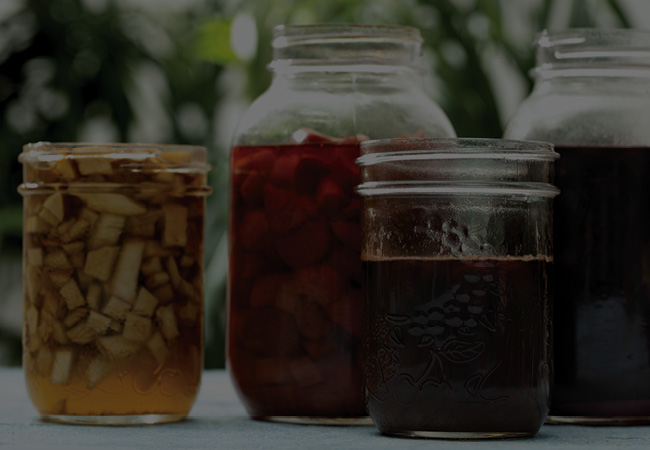 Four jars on a counter filled with different fruit shrubs