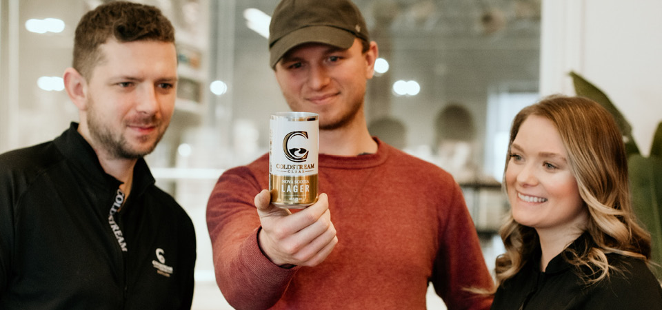 The three Griffin siblings stand together holding a can of Coldstream lager.