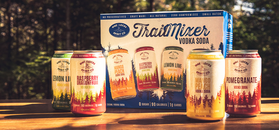 Image of Nine Locks Trail Mixer vodka soda pack on a table with the woods in the background