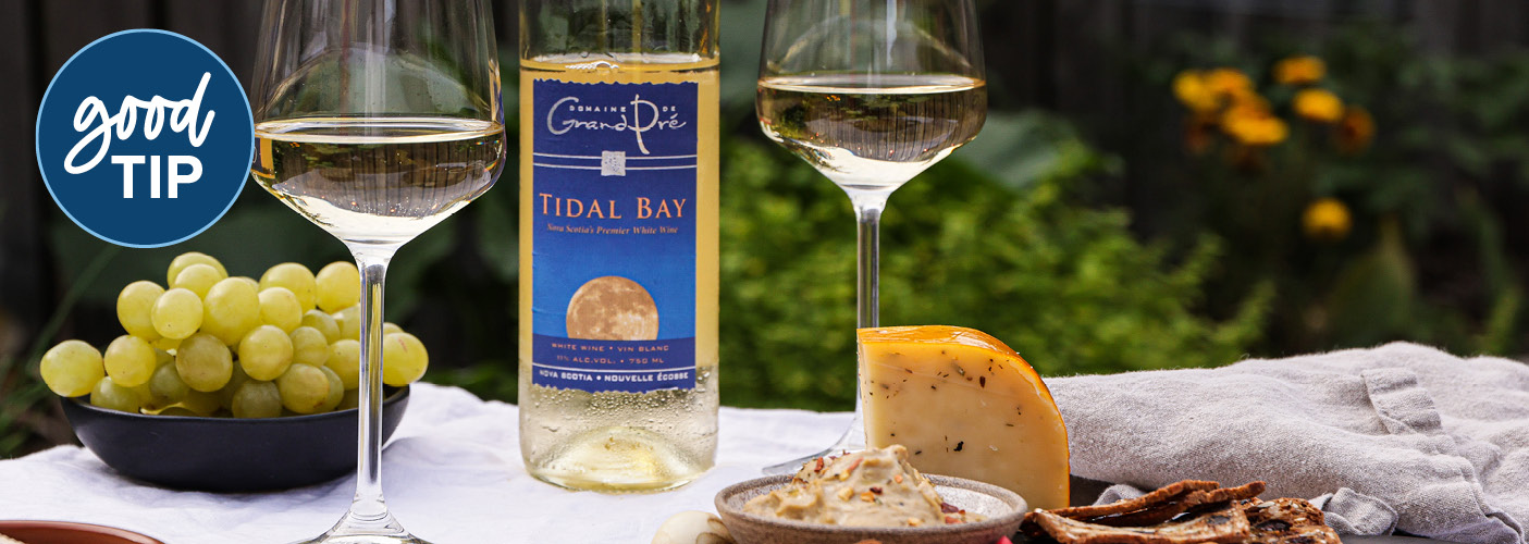 Two wine glasses with a bottle of Tidal Bay between them on a board with grapes and cheese.