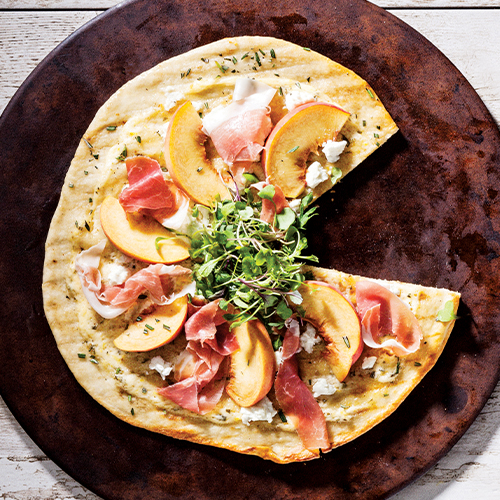 Morris East's Peach and Prosciutto Pizza on a pizza stone with a slice missing