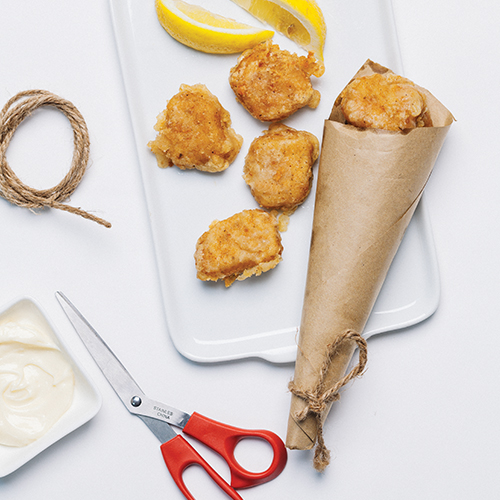 A paper cone container filled with fish bites accompanied by lemon wedges