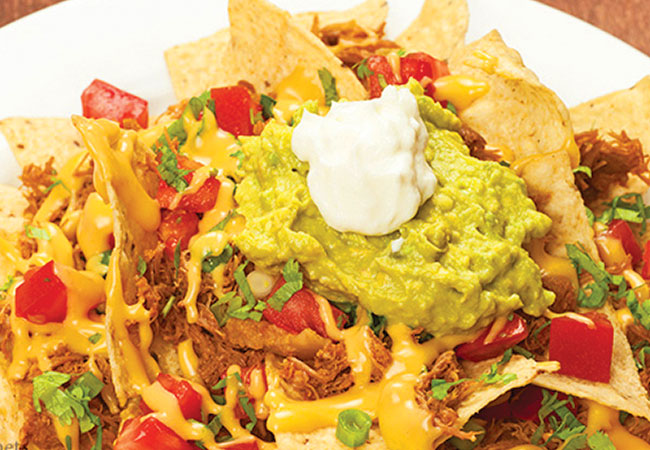 Loaded nachos topped with veggies, pull pork, cheese sauce and guacamole