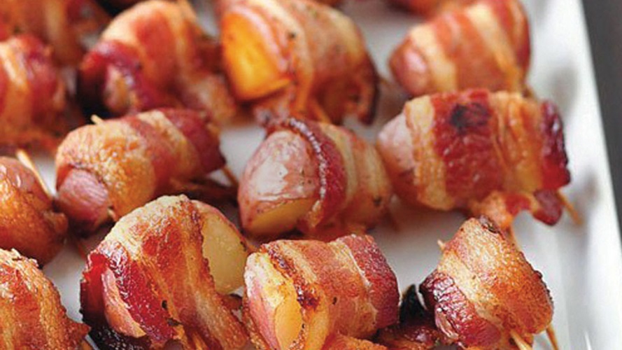 Rows of bacon wrapped potato bites on a white platter