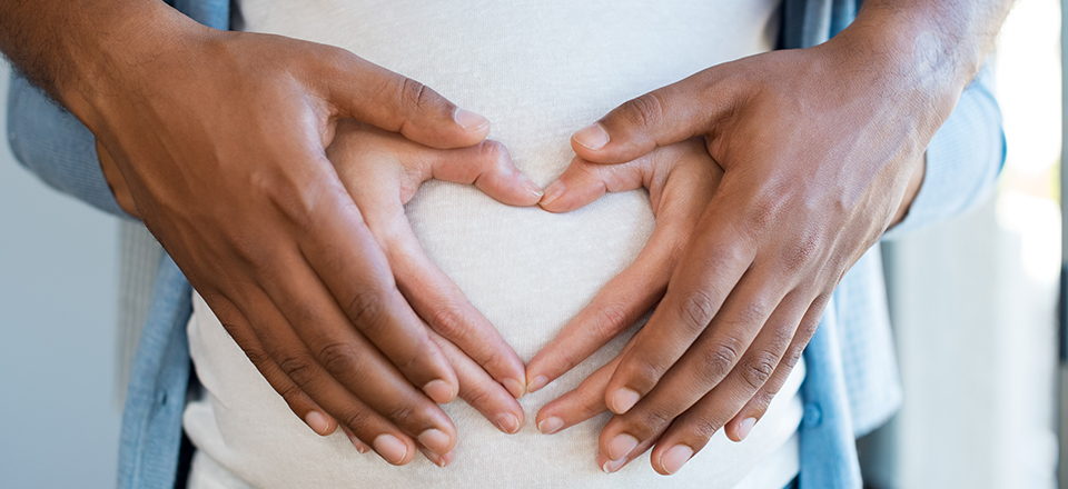Hands making a heart over a pregnant belly 